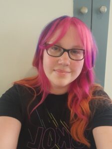 Picture of me. My hair is pink and orange, I'm wearing dark purple glasses and a Minnesota Vikings Pride Skol t-shirt.